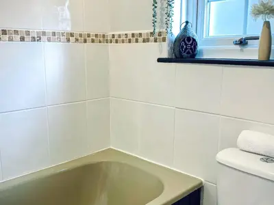 a bath tub in a white tiled bathroom at Hawthorn in Bude