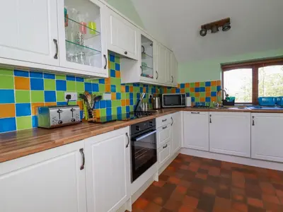 a kitchen with white cabinets and colorful tiles on the wall at The Old Piggery in Truro