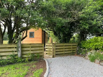 a small wooden cabin with a fence and trees at Kilden Hut - Perranwell Station in Perranwell