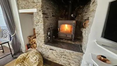 a stone fireplace in a living room with a stove at Sophie's Cottage in Philleigh