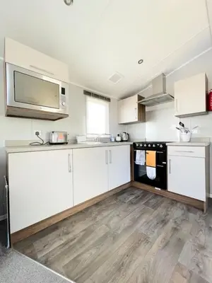 a kitchen with white cabinets and a microwave at Ocean Breeze-Haven Perran Sands Holiday Park in Perranporth