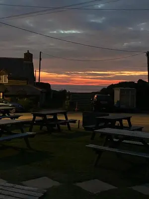 a group of picnic tables with a sunset in the background at Bossiney Lodge Apartment in Tintagel
