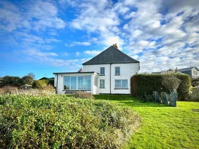 a white house on a grassy field with a sky at Old Chapel House in Tintagel