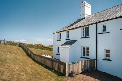 a white house with a fence next to it at Trevigue Cottage in Bude