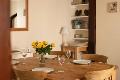 a wooden table with plates and glasses and yellow flowers at Honeysuckle Cottage in Saint Minver
