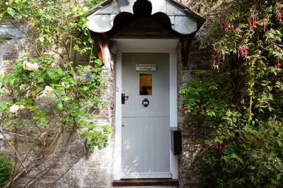 a white door in a brick building with plants at Honeysuckle Cottage in Saint Minver
