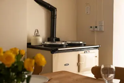 a kitchen with a stove and a table with yellow flowers at Honeysuckle Cottage in Saint Minver