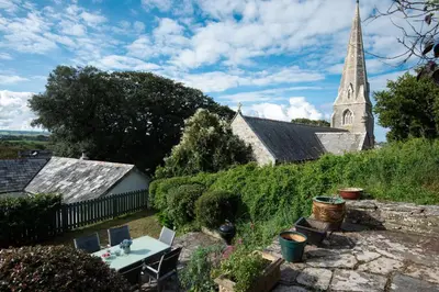 a church with a steeple and a table in a garden at Honeysuckle Cottage in Saint Minver