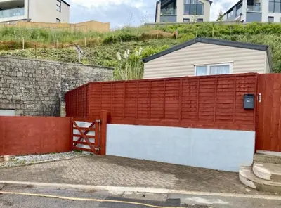 a red and white fence with a building behind it at Cabin by Beach & Nature Reserve Mon & Fri Check in Days Swanpool Falmouth Cornwall in Falmouth