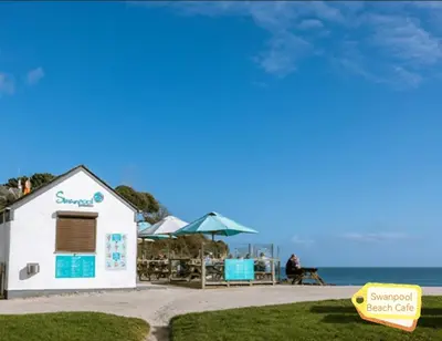 a small white building next to the beach at Cabin by Beach & Nature Reserve Mon & Fri Check in Days Swanpool Falmouth Cornwall in Falmouth