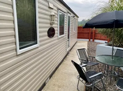 a patio with two chairs and a table and an umbrella at Cabin by Beach & Nature Reserve Mon & Fri Check in Days Swanpool Falmouth Cornwall in Falmouth