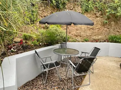 a table and chairs with an umbrella on a patio at Cabin by Beach & Nature Reserve Mon & Fri Check in Days Swanpool Falmouth Cornwall in Falmouth