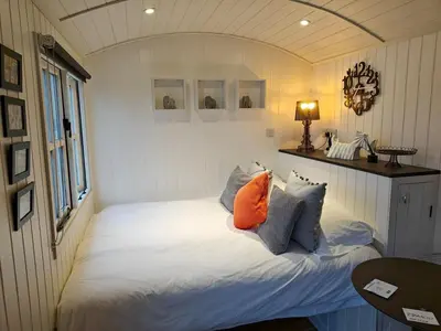 a bedroom with a bed with an orange pillow at Luxury Countryside Shepherds Hut with Hot Tub in Saint Mawgan