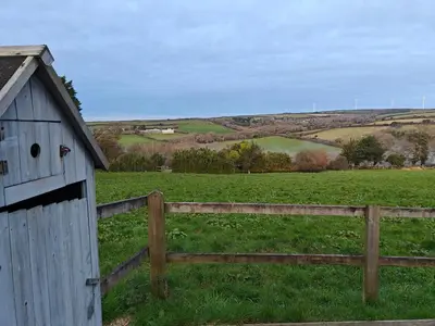 a barn in a field next to a fence at Luxury Countryside Shepherds Hut with Hot Tub in Saint Mawgan