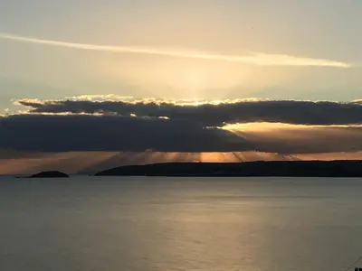 a sunset over a body of water with the sun hiding behind clouds at Ocean View at Kenwyn in Torpoint
