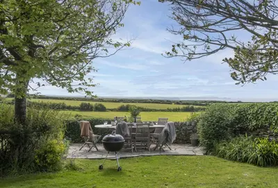a patio with a table and chairs and a grill at Besloe in Delabole