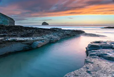 a sunset over a beach with rocks and the ocean at Besloe in Delabole