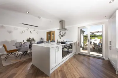 a kitchen with white cabinets and a table with chairs at Highfield Barton in Camborne