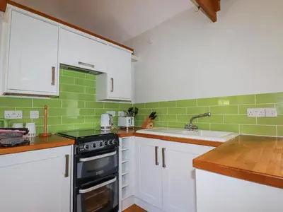a kitchen with white cabinets and green tiles at Rose's Stable in Truro