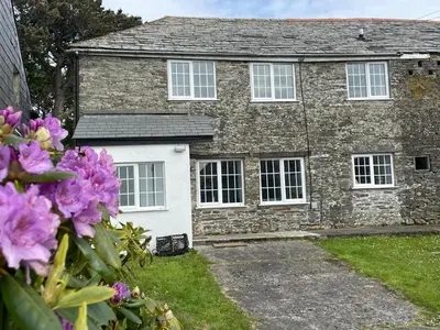 an old stone house with white doors and purple flowers at Menadue Cottage, Trenale Lane, Tintagel, Cornwall in Treknow