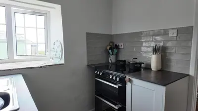 a kitchen with a black stove and a window at Menadue Cottage, Trenale Lane, Tintagel, Cornwall in Treknow