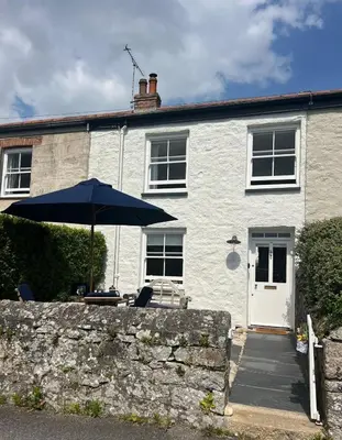 a white house with an umbrella and chairs at Stunning seaside cottage Charlestown harbour in Charlestown