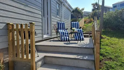 three chairs and a table on a porch with a fence at D26 Vu-An-Tecca, Riviere Towans in Hayle