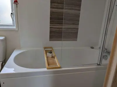 a bathroom with a bath tub with a shower and a toilet at 63 The Lea with decking Trevella Holiday Park in Crantock