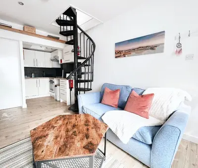 a living room with a blue couch and a spiral staircase at SURF PAD in St Ives, 1 Bed Apartment , 400M to Beach & Harbour in St Ives