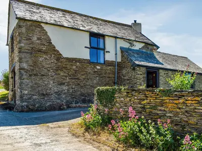 an old stone house with blue windows and flowers at Carriage House in Mawgan Porth