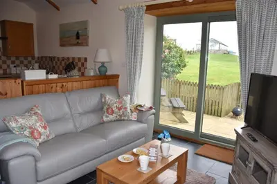 a living room with a gray couch and a television at Beech cottage is a beautiful 1 bed cottage in Saint Ewe