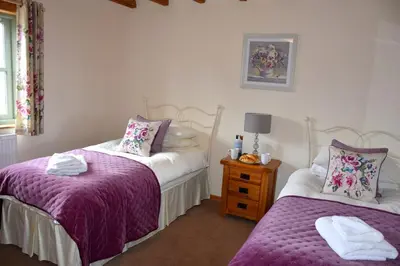 a bedroom with two beds with purple sheets and a table at Hawthorn Cottage Luxury stone Built Cottage in Tregoney