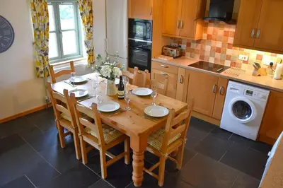 a kitchen with a wooden table with chairs and a washing machine at Hawthorn Cottage Luxury stone Built Cottage in Tregoney
