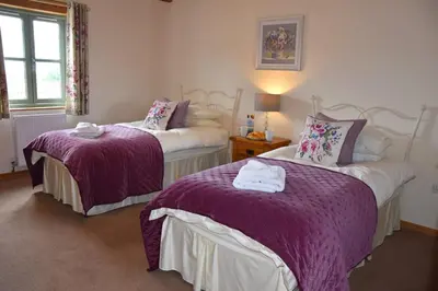 two beds in a room with purple and white sheets at Hawthorn Cottage Luxury stone Built Cottage in Tregoney