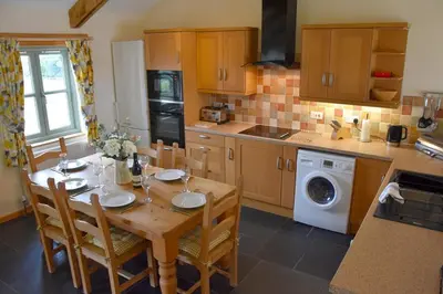 a kitchen with a wooden table with chairs and a washing machine at Hawthorn Cottage Luxury stone Built Cottage in Tregoney