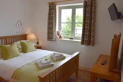 a bedroom with a bed with a dog sitting in a window at Hazel - 3 Bed accessible holiday cottages in Tregoney
