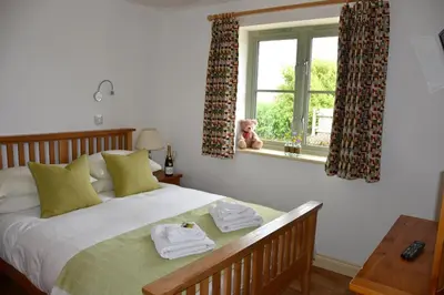 a bedroom with a bed with towels and a dog looking out the window at Hazel - 3 Bed accessible holiday cottages in Tregoney