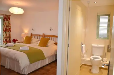 a bedroom with a bed and a bathroom with a toilet at Hazel - 3 Bed accessible holiday cottages in Tregoney