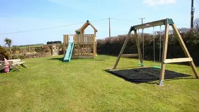 a playground with two swings in a yard at Hazel - 3 Bed accessible holiday cottages in Tregoney