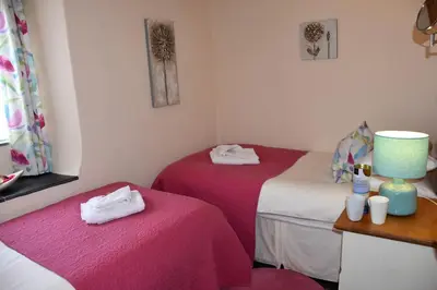 two twin beds in a room with pink sheets at Oak Cottage in Tregoney