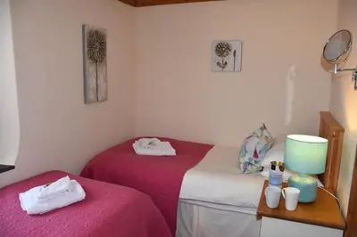two beds in a room with pink and white sheets at Oak Cottage in Tregoney