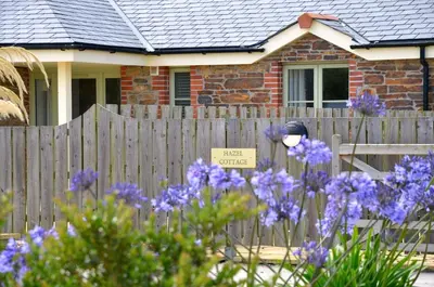 a fence in front of a house with purple flowers at Willow Beautiful 3 bed accessible holiday cottages in Tregoney
