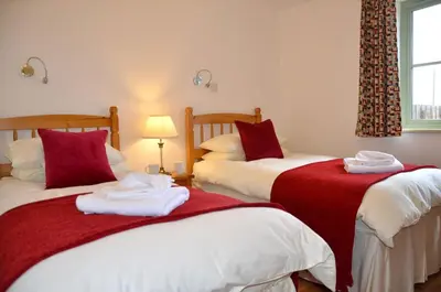 a bedroom with two beds with red and white sheets at Willow Beautiful 3 bed accessible holiday cottages in Tregoney