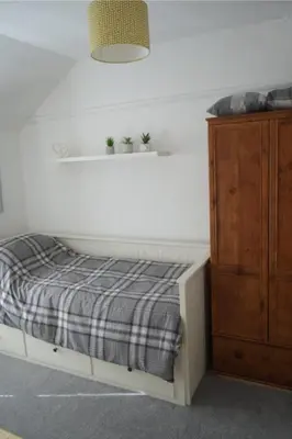 a bed with a plaid blanket next to a wooden cabinet at Dunlin Cottage in Penryn