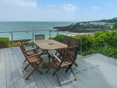 a wooden table and chairs on a deck with the ocean at Coastguards in Porthscatho
