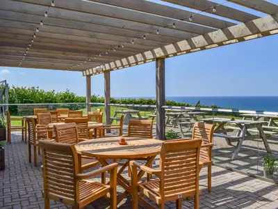 a patio with wooden tables and chairs and the ocean at Little Palms in Bude