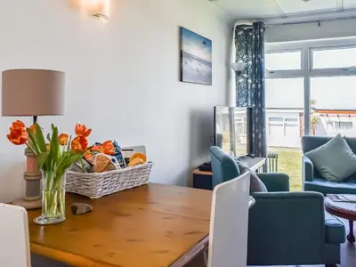 a dining room table with a vase of flowers on it at Little Palms in Bude