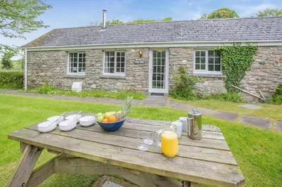 a wooden picnic table with a bowl of fruit and orange juice at 2 Bed in Advent oc-o31790 in Lanteglos