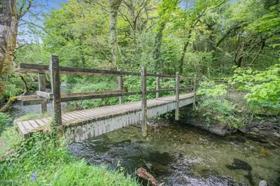 a wooden bridge over a stream in a forest at 2 Bed in Advent oc-o31790 in Lanteglos