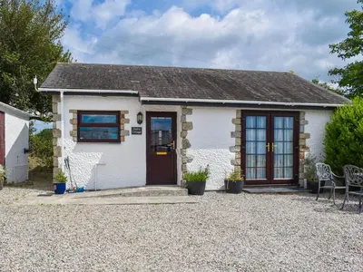 a white cottage with a red door and chairs at Dairy Cottage - Uk49834 in Lanivet